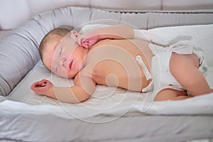 A baby boy sleeps in a cocoon on a cot. A newborn baby in a diaper is lying naked on the bed