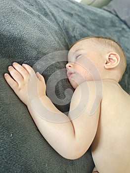 A baby boy sleeps soundly on his stomach during the day on a gray blanket photo