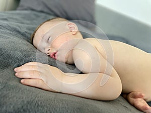 A baby boy sleeps soundly on his stomach during the day on a gray blanket photo