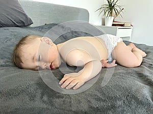 A baby boy sleeps soundly on his stomach during the day on a gray blanket photo