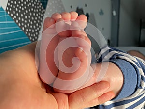 Baby boy small feet, no socks, little toes, playing in bed, blue stripes pijamas