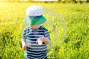 Baby boy standing in grass on the fieald with dandelions