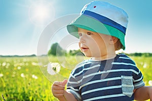 Baby boy standing in grass on the fieald with dandelions