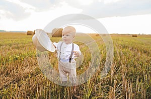 A baby boy with a straw hat walks in the field. Wheat field sunset