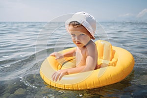 Baby boy swims with an inflatable yellow circle in the sea on a sunny day. The kid learns to swim and enjoys the game.