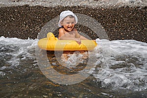 Baby boy swims with an inflatable yellow circle in the sea on a sunny day. The kid learns to swim near the shore and