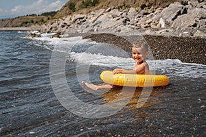 Baby boy swims with an inflatable yellow circle in the sea on a sunny day. The kid learns to swim near the shore and