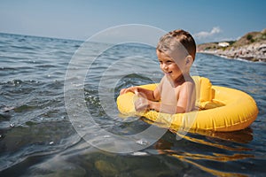 Baby boy swims in a yellow inflatable circle in the sea. The child is happy and laughing.