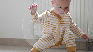 Baby boy taking first steps . Little child girl walking on gets up and starts walking at home. Barefoot legs on kitchen.