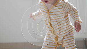 Baby boy taking first steps . Little child girl walking on gets up and starts walking at home. Barefoot legs on kitchen.