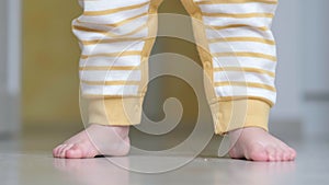 Baby boy taking first steps . Unrecognizable Little child girl walking on white floor at home. Barefoot legs on kitchen.