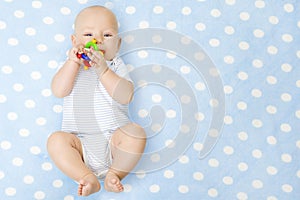 Baby Boy with Teether Toy In Mouth Lying over Blue Background, Happy