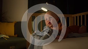 Baby boy toddler crawling in crib at kids nursery room at night.