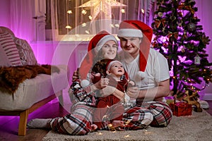 Baby boy toddler with his mother and father are sitting by the Christma