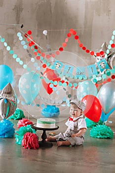 Baby boy touching his first birthday cake. Making messy cakesmash in decorated studio location