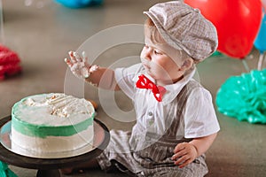 Baby boy touching his first birthday cake. Making messy cakesmash in decorated studio location