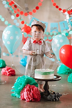 Baby boy touching his first birthday cake. Making messy cakesmash in decorated studio location