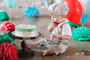 Baby boy touching his first birthday cake. Making messy cakesmash in decorated studio location