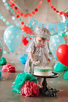 Baby boy touching his first birthday cake. Making messy cakesmash in decorated studio location