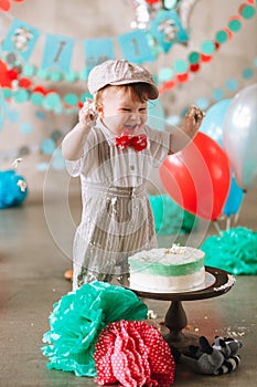 Baby boy touching his first birthday cake. Making messy cakesmash in decorated studio location