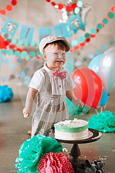 Baby boy touching his first birthday cake. Making messy cakesmash in decorated studio location