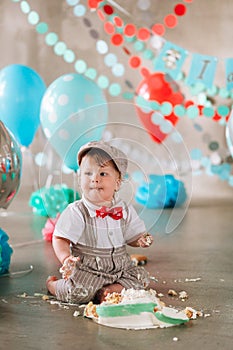 Baby boy touching his first birthday cake. Making messy cakesmash in decorated studio location