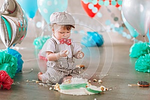 Baby boy touching his first birthday cake. Making messy cakesmash in decorated studio location