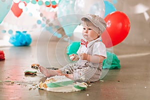 Baby boy touching his first birthday cake. Making messy cakesmash in decorated studio location. Dirty bare foot