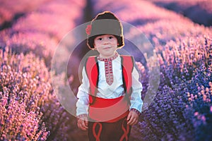 Baby boy in traditional Bulgarian folklore costume in lavender field. Working peasant during lavender harvest