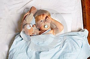 Baby boy waking up in the bed with toy, wipe eyes