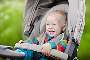 Baby boy in warm colorful knitted jacket sitting in modern stroller on a walk in a park. Child in buggy. Little kid in a pushchair