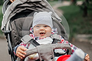 Baby boy in warm colorful knitted jacket sitting in modern stroller on a walk in a park. Child in buggy. Little kid in a