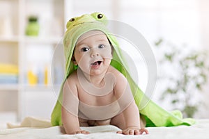 Baby boy wearing green towel in sunny bedroom. Newborn child relaxing after bath or shower.