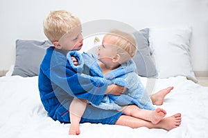 Baby brothers sitting on bed in bathrobe and playing. Siblings in blue bathrobe. Baby care concept, banner copy space