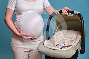 Baby car seat in pregnant woman, studio shot on blue background