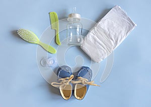 Baby care accessories, newborn baby diaper, pacifier, comb and hair brush, bottle and little boy shoes on a blue background. Wish