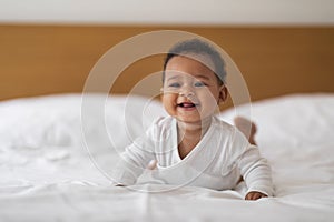 Baby Care Concept. Adorable Black Infant Child Relaxing On Bed At Home