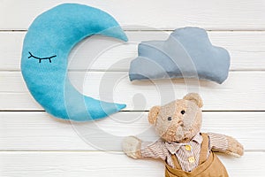 Baby care concept with moon pillow, clouds, teddy bear and toy for sleep of newborn on white wooden background top view
