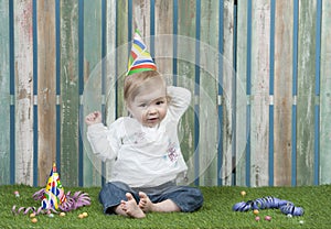 Baby with carnival hat seated in the garden