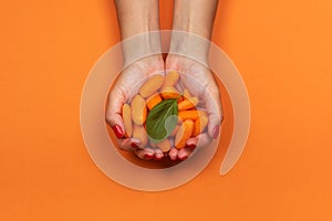 Baby carrot in girls hands on orange background