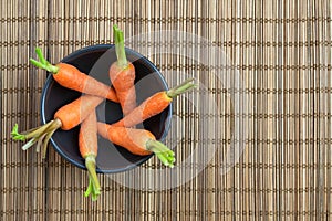 Baby carrots arranged in a circle in black bowl over brown bamboo mat.