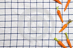 Baby carrots over white table cloth with blue grid pattern.