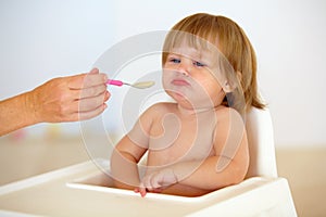 Baby, chair and eating food or unhappy mood for health meal, childhood development or upset. Hand, spoon and feed seat