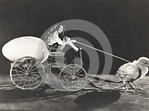 Baby chick pulling cart with woman and giant egg