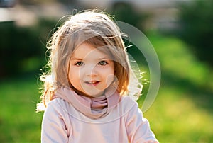 Baby child on the green grass in summer park. Baby face closeup. Funny little child close up portrait. Blonde kid