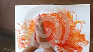 Baby child is painting with hands using colored finger gel paints, heart shape