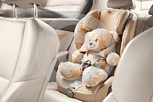 Baby child seat car. A beige teddy bear is fastened with seat belts in a car seat. Travel by car