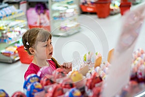 Baby chooses a gift.A little girl is looking at the shelf with sweets in the store. The child wants to buy chocolate eggs in the