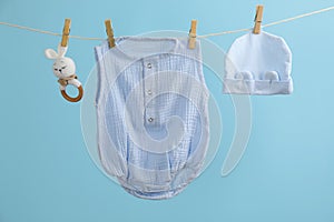 Baby clothes and accessories hanging on washing line against light blue background