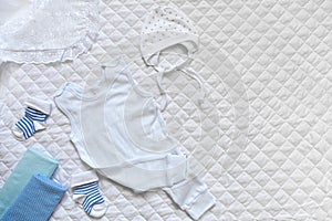 Baby clothes bonnet, bodysuit, socks, diaper, corner on a white textured background.